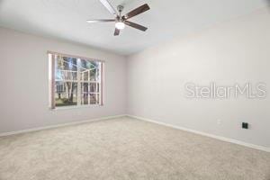 carpeted empty room featuring a ceiling fan and baseboards