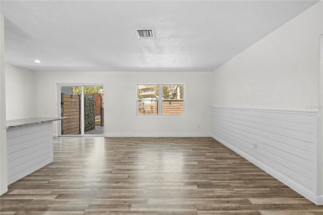 empty room with a wainscoted wall, wood finished floors, and visible vents