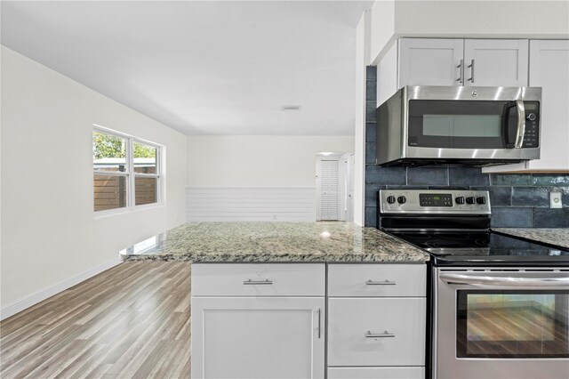 kitchen with appliances with stainless steel finishes, light stone countertops, light wood-type flooring, white cabinetry, and backsplash