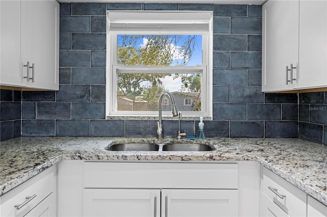 kitchen featuring backsplash, a sink, white cabinetry, and light stone countertops