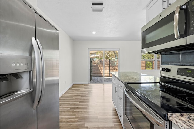 kitchen with visible vents, white cabinetry, appliances with stainless steel finishes, light wood-type flooring, and light stone countertops