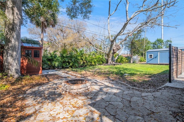 view of yard with an outdoor fire pit, fence, an outbuilding, and a shed