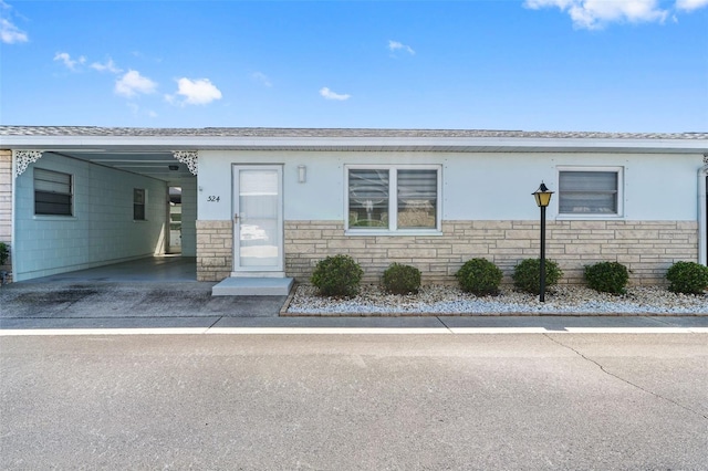 view of front facade with an attached carport, stone siding, driveway, and stucco siding