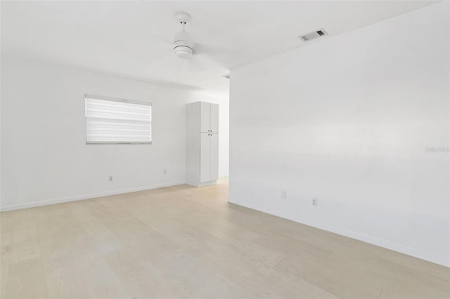 spare room with a ceiling fan, light wood-type flooring, visible vents, and baseboards