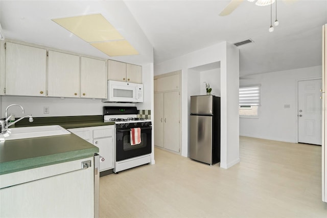 kitchen featuring range with gas stovetop, visible vents, white microwave, freestanding refrigerator, and a sink