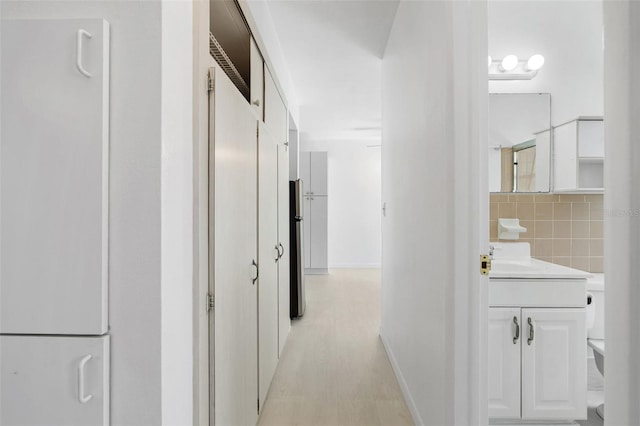 corridor with light wood finished floors, a sink, and tile walls