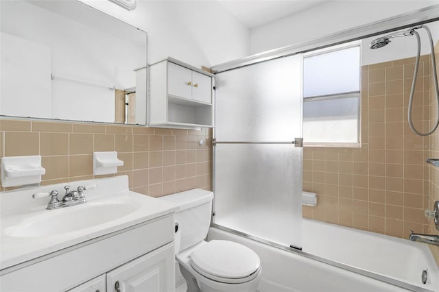 bathroom featuring toilet, bath / shower combo with glass door, tile walls, and vanity