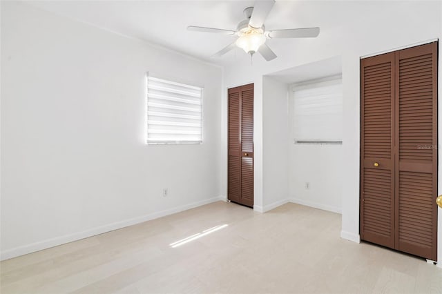 unfurnished bedroom with light wood-type flooring, ceiling fan, baseboards, and two closets