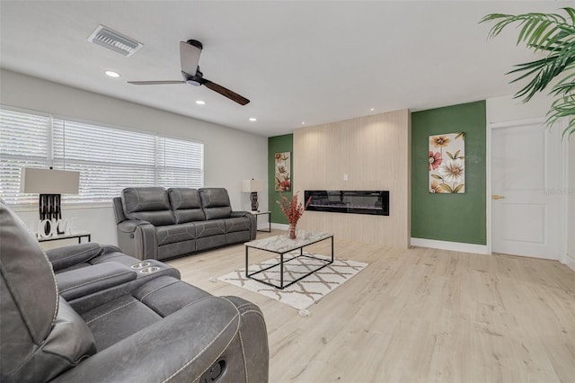 living room with wood finished floors, a glass covered fireplace, visible vents, and baseboards