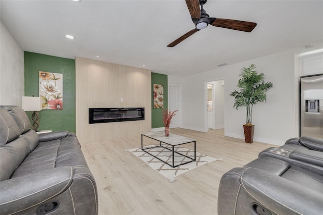 living room featuring light wood-style floors, a glass covered fireplace, recessed lighting, and a ceiling fan