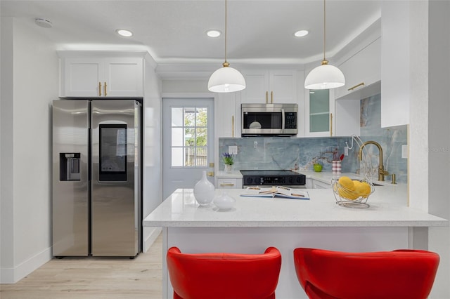 kitchen featuring tasteful backsplash, white cabinets, a peninsula, stainless steel appliances, and a sink