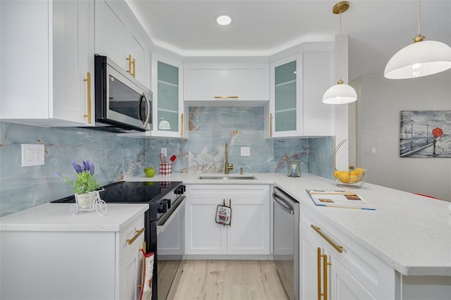 kitchen with light wood finished floors, decorative backsplash, appliances with stainless steel finishes, a sink, and a peninsula