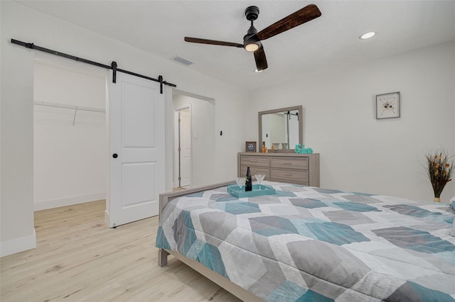 bedroom with ceiling fan, a barn door, visible vents, light wood-style floors, and a walk in closet