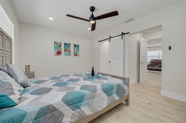 bedroom featuring a barn door, visible vents, baseboards, light wood-style flooring, and recessed lighting