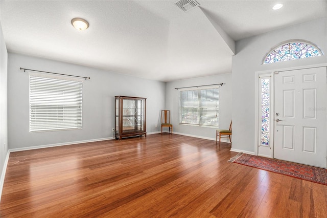 foyer entrance with baseboards, visible vents, a textured ceiling, and hardwood / wood-style floors