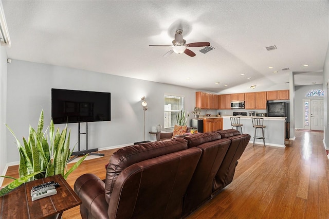 living area with lofted ceiling, visible vents, and wood finished floors