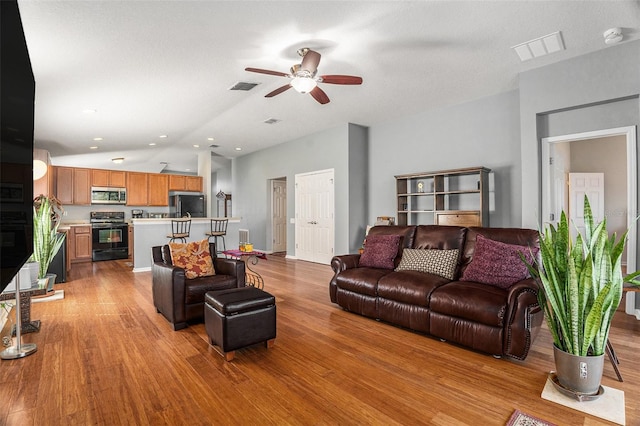 living room with light wood-type flooring, lofted ceiling, visible vents, and ceiling fan