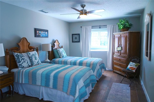 bedroom featuring dark wood-style floors, visible vents, a textured ceiling, and a ceiling fan