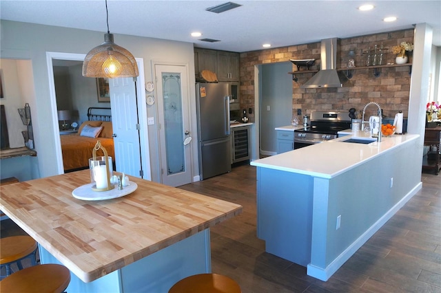 kitchen with stainless steel appliances, dark wood-style flooring, a sink, visible vents, and wall chimney exhaust hood