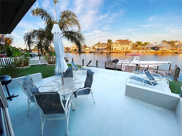 view of patio / terrace featuring a boat dock, a water view, fence, and outdoor dining space