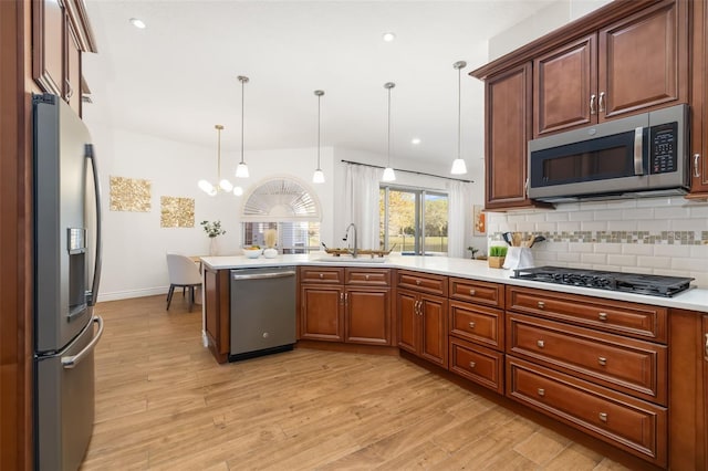 kitchen with stainless steel appliances, a sink, a peninsula, and light wood finished floors