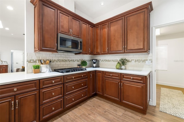 kitchen featuring light countertops, stainless steel microwave, light wood finished floors, and black gas stovetop