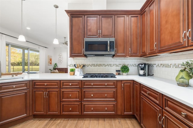 kitchen with stainless steel microwave, light countertops, light wood-type flooring, backsplash, and black gas stovetop