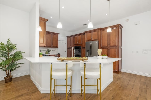 kitchen featuring a peninsula, a breakfast bar, light wood-style floors, appliances with stainless steel finishes, and backsplash