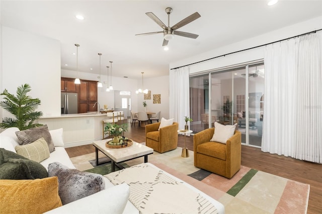 living room featuring recessed lighting, light wood finished floors, and ceiling fan with notable chandelier