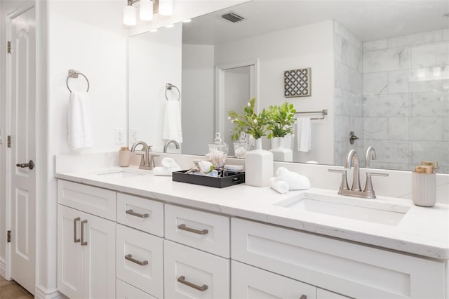 full bathroom featuring visible vents, a sink, a tile shower, and double vanity