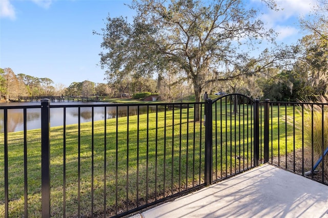 view of gate with a water view, a lawn, and fence