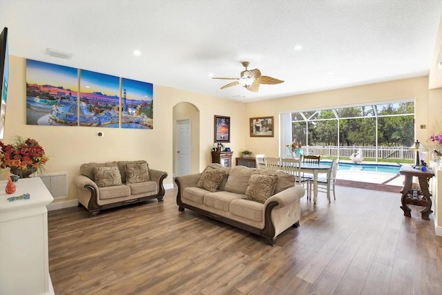 living area with arched walkways, wood finished floors, a sunroom, visible vents, and a ceiling fan