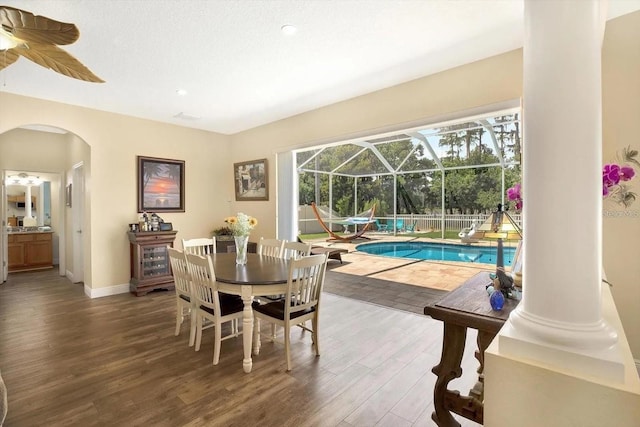 dining room with arched walkways, a sunroom, a textured ceiling, wood finished floors, and baseboards