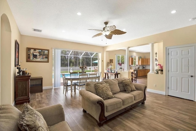 living room with decorative columns, visible vents, baseboards, a ceiling fan, and wood finished floors