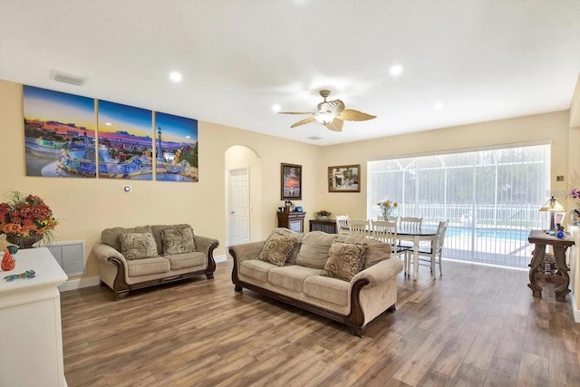 living room featuring a ceiling fan, visible vents, arched walkways, and wood finished floors