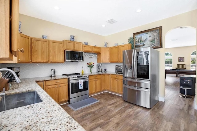 kitchen featuring light stone counters, stainless steel appliances, visible vents, a sink, and wood finished floors