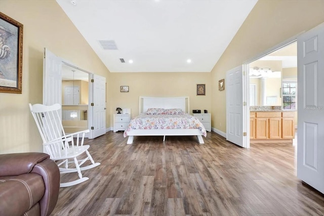 bedroom with lofted ceiling, visible vents, ensuite bath, wood finished floors, and baseboards