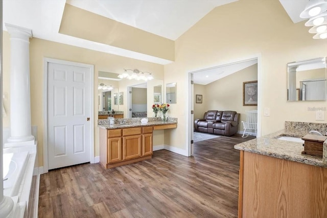 full bath with two vanities, wood finished floors, vaulted ceiling, ornate columns, and a bath