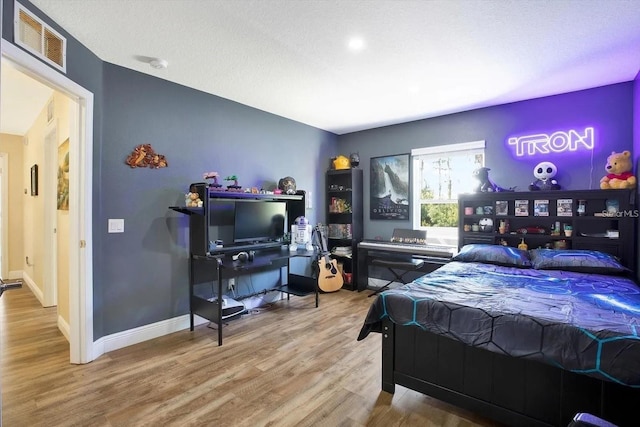 bedroom with a textured ceiling, wood finished floors, visible vents, and baseboards