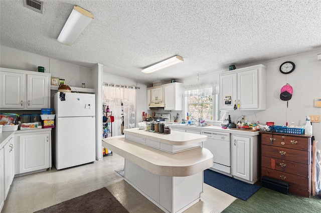 kitchen featuring white appliances, white cabinetry, visible vents, light countertops, and a center island