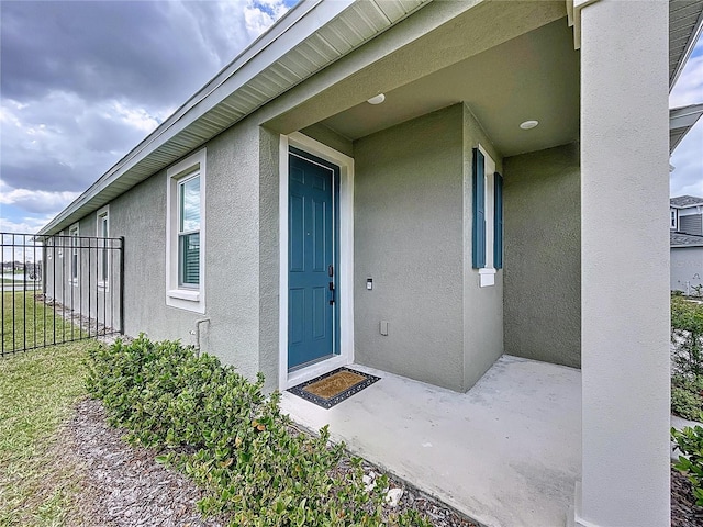 view of exterior entry with fence and stucco siding