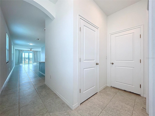 hallway with light tile patterned floors, baseboards, visible vents, and arched walkways