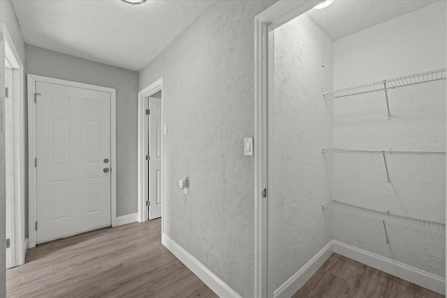 hallway with baseboards, wood finished floors, and a textured wall