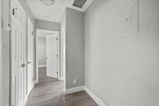 hall featuring electric panel, visible vents, baseboards, and wood finished floors