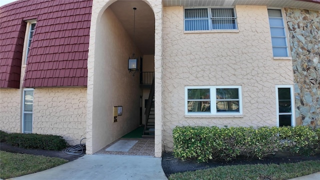 view of exterior entry with a tiled roof, mansard roof, and stucco siding