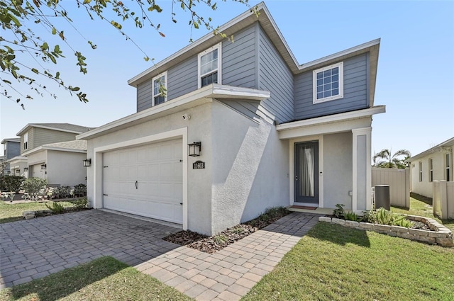 view of front of property with decorative driveway, an attached garage, fence, and stucco siding