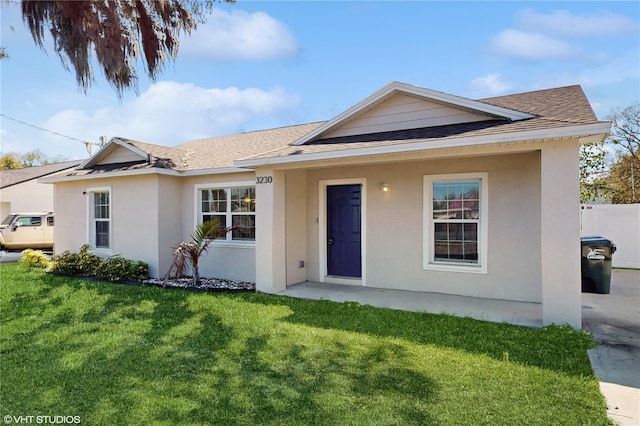 ranch-style home with a front yard, roof with shingles, fence, and stucco siding