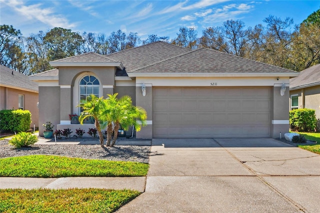 ranch-style house with an attached garage, roof with shingles, concrete driveway, and stucco siding