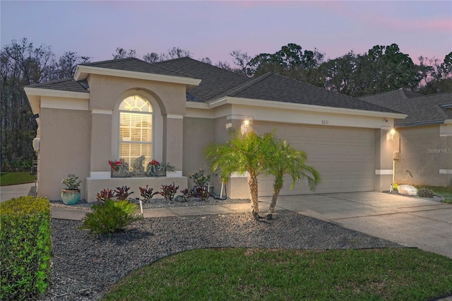 ranch-style house featuring an attached garage, driveway, a shingled roof, and stucco siding