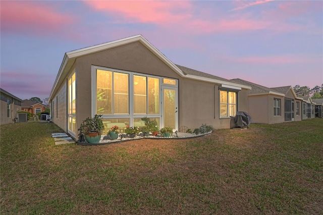 back of house at dusk featuring a lawn and stucco siding